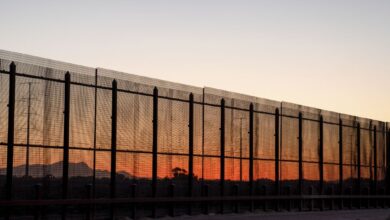 US border fence at sunset with silhouetted mountains