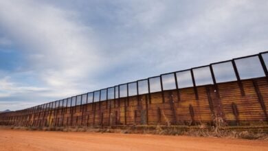 Long border fence beside dirt road under cloudy sky